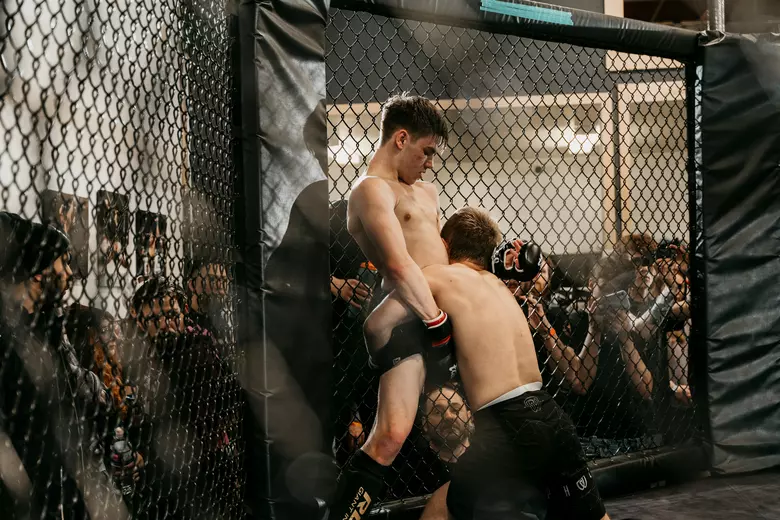 Fighters grappling against the fence securing a guillotine choke